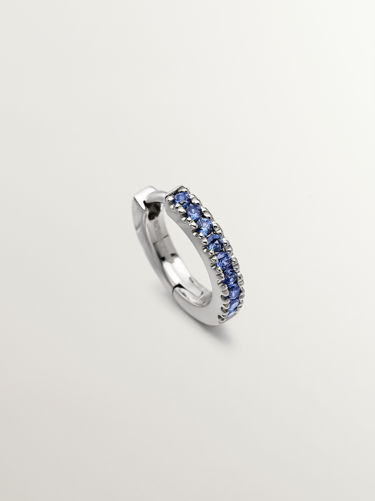 Individual 9K white gold hoop earring with blue sapphires.