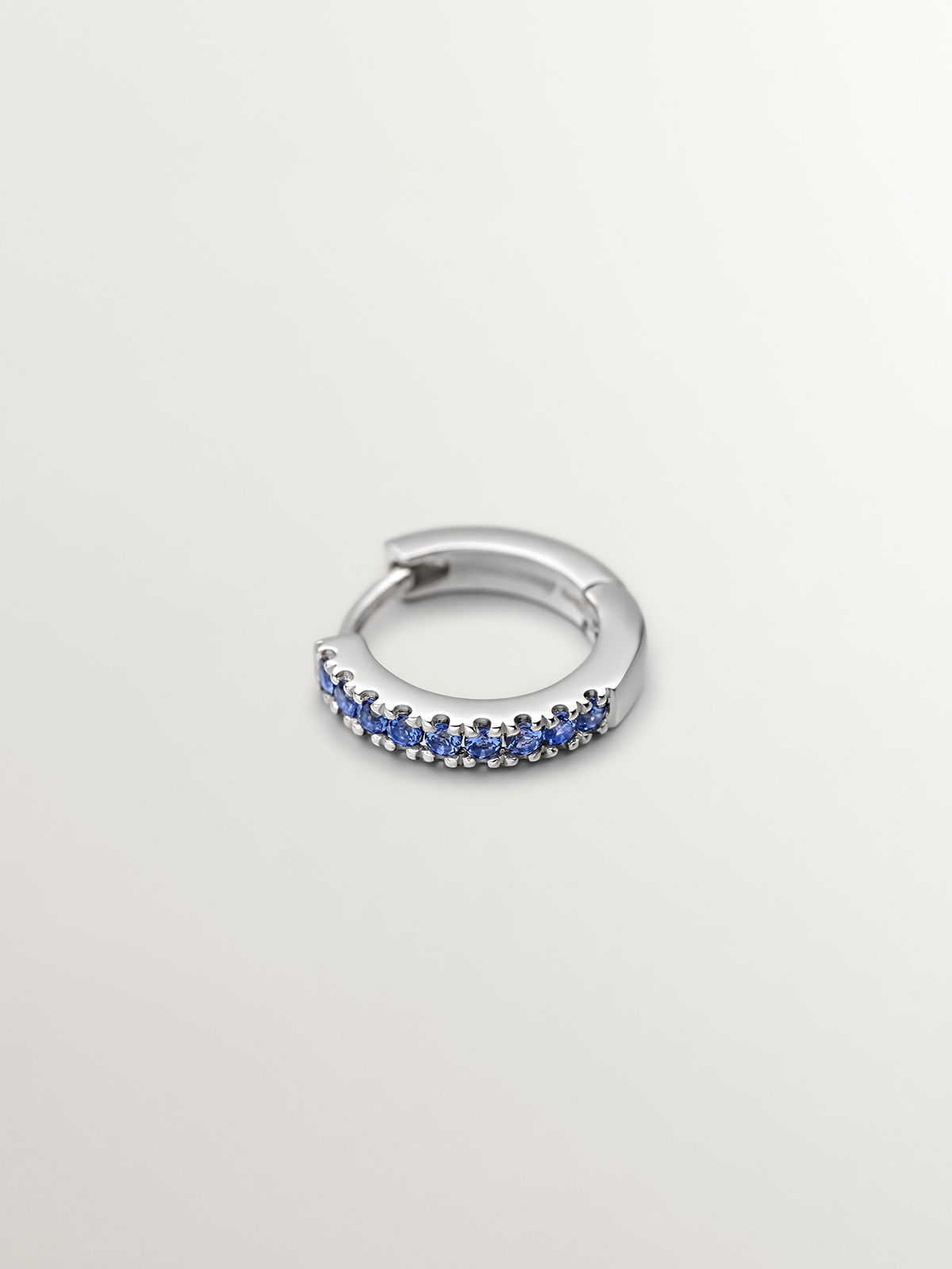 Individual 9K white gold hoop earring with blue sapphires.